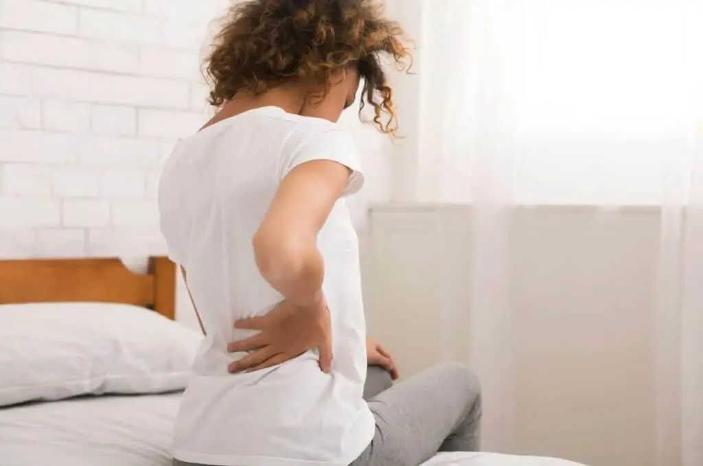 A woman sitting on top of her bed with her hands behind her back.