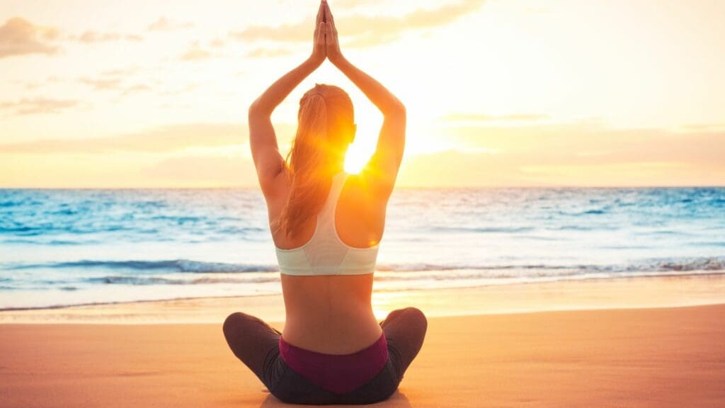 A woman sitting on the beach doing yoga.