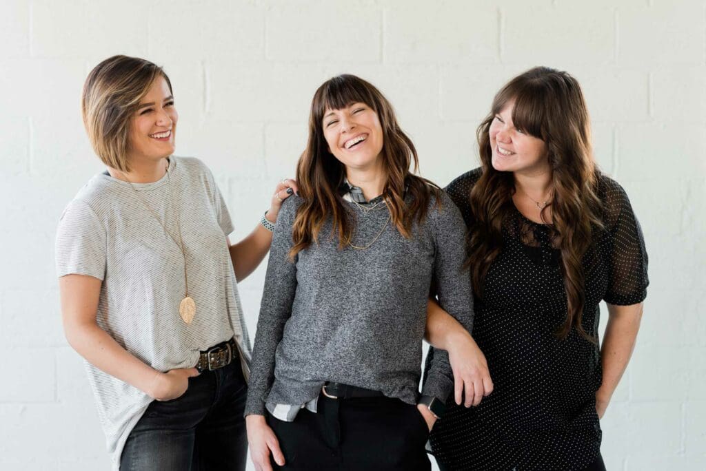 Three women posing for a picture in front of a wall.