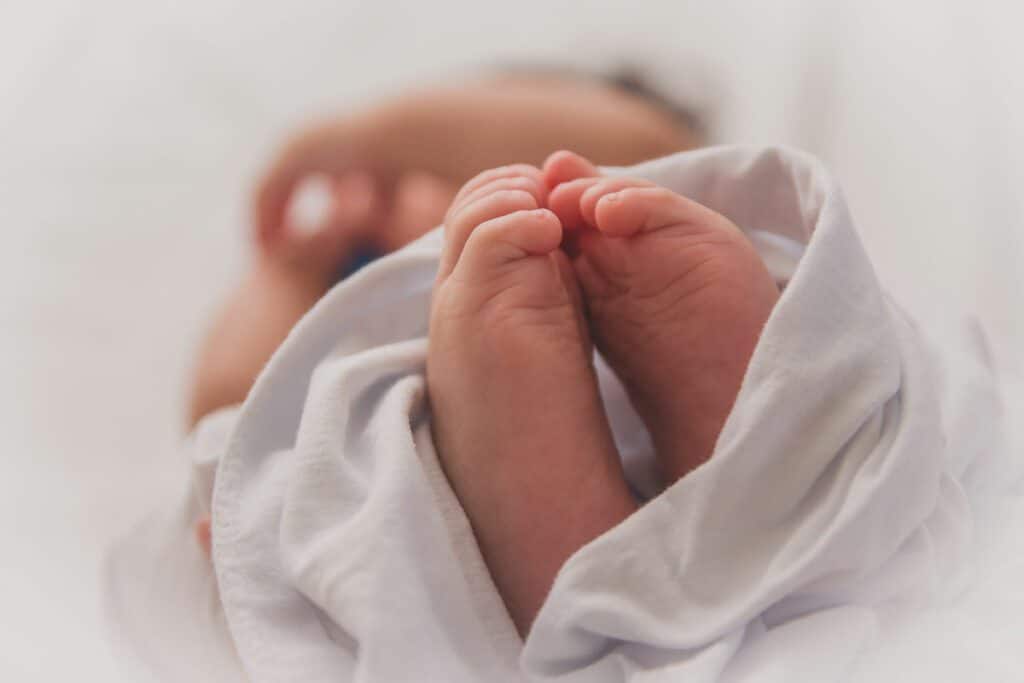 A baby is wrapped in a blanket and holding its feet.