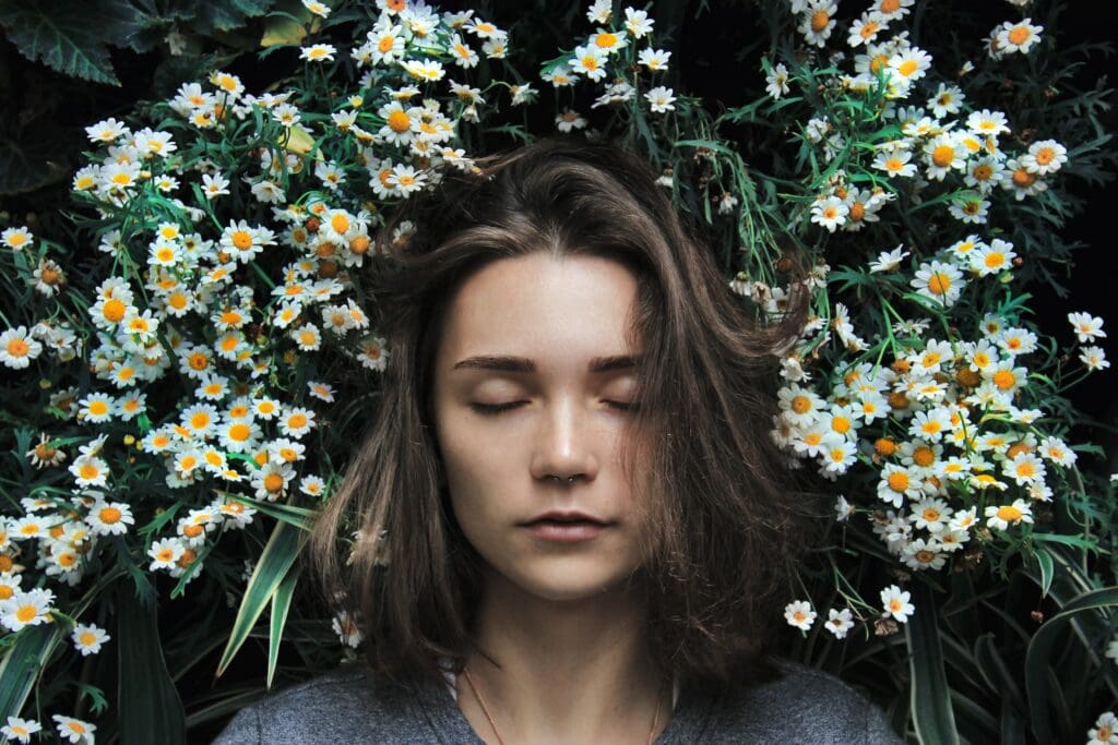 A woman with her eyes closed in front of some flowers.