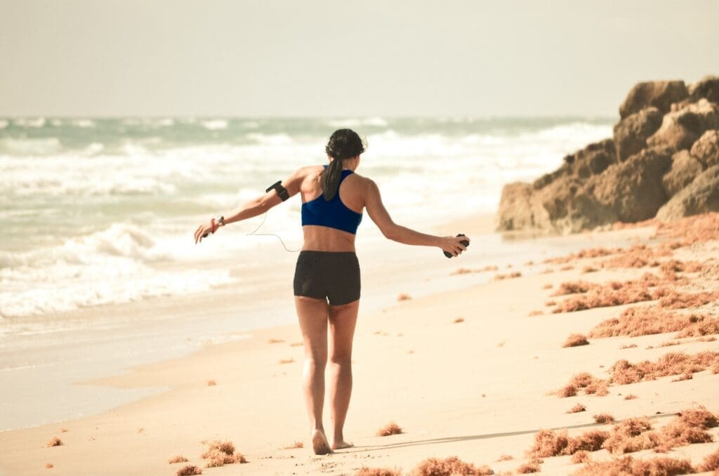 A woman walking on the beach with her arms outstretched.