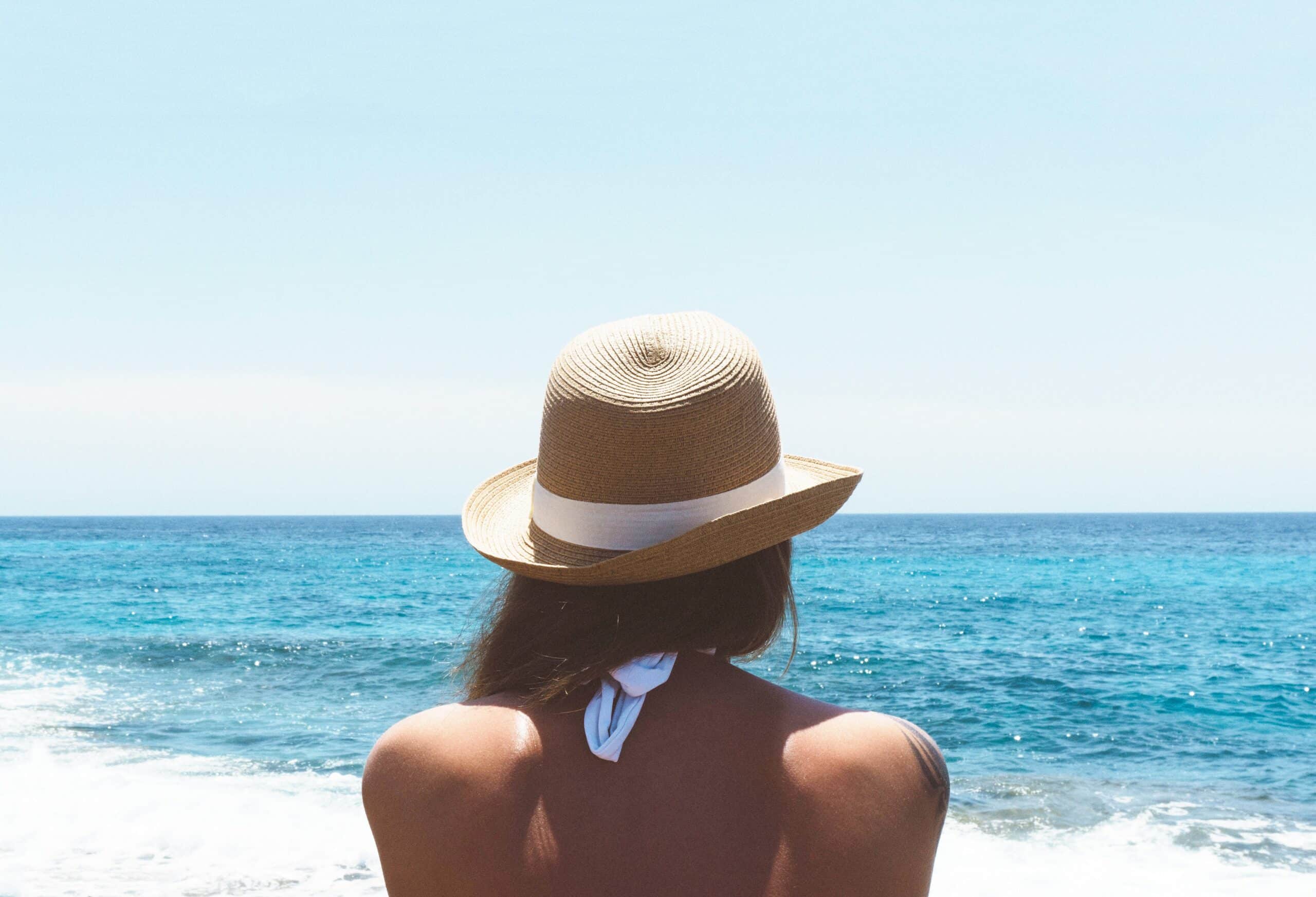 A woman sitting on the beach wearing a hat.