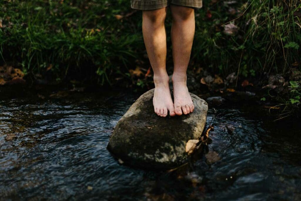 A person standing on top of a rock in the water.