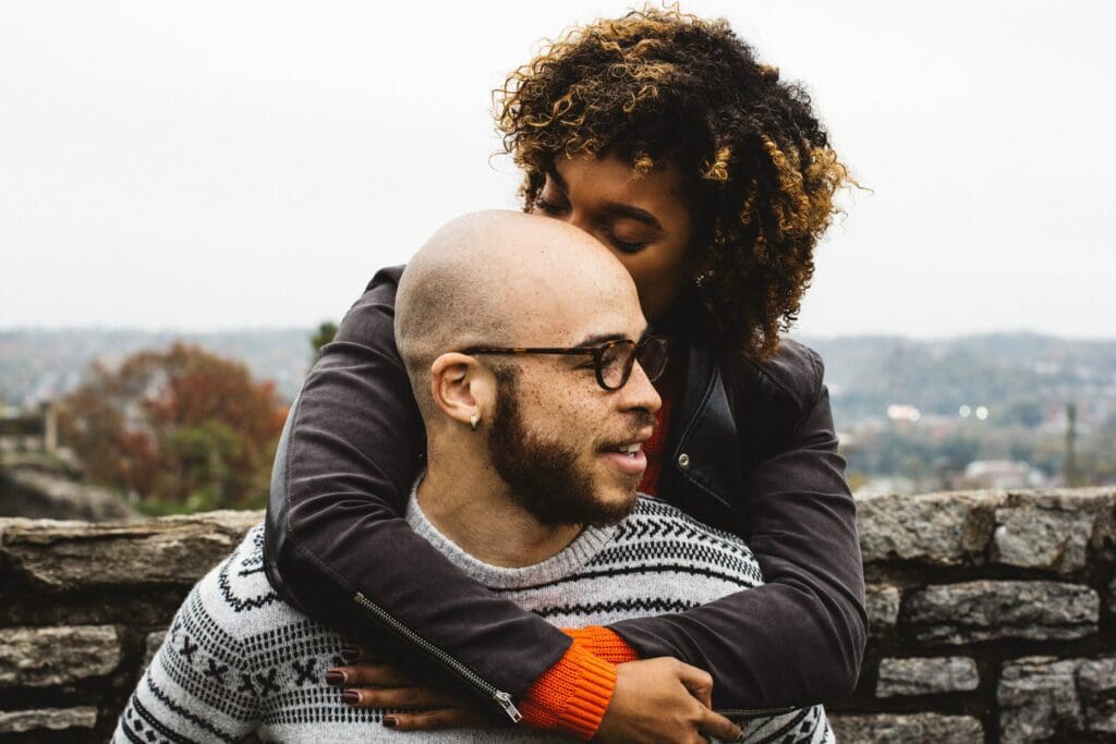 A man and woman hugging each other on top of a hill.