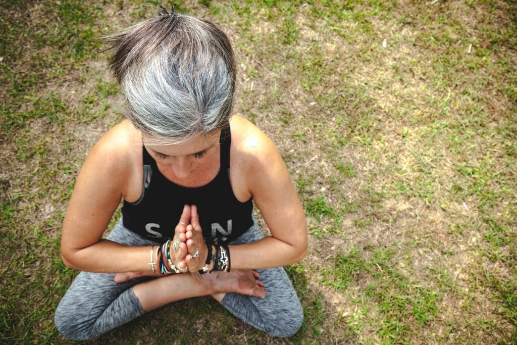 A woman sitting on the ground with her hands in prayer.