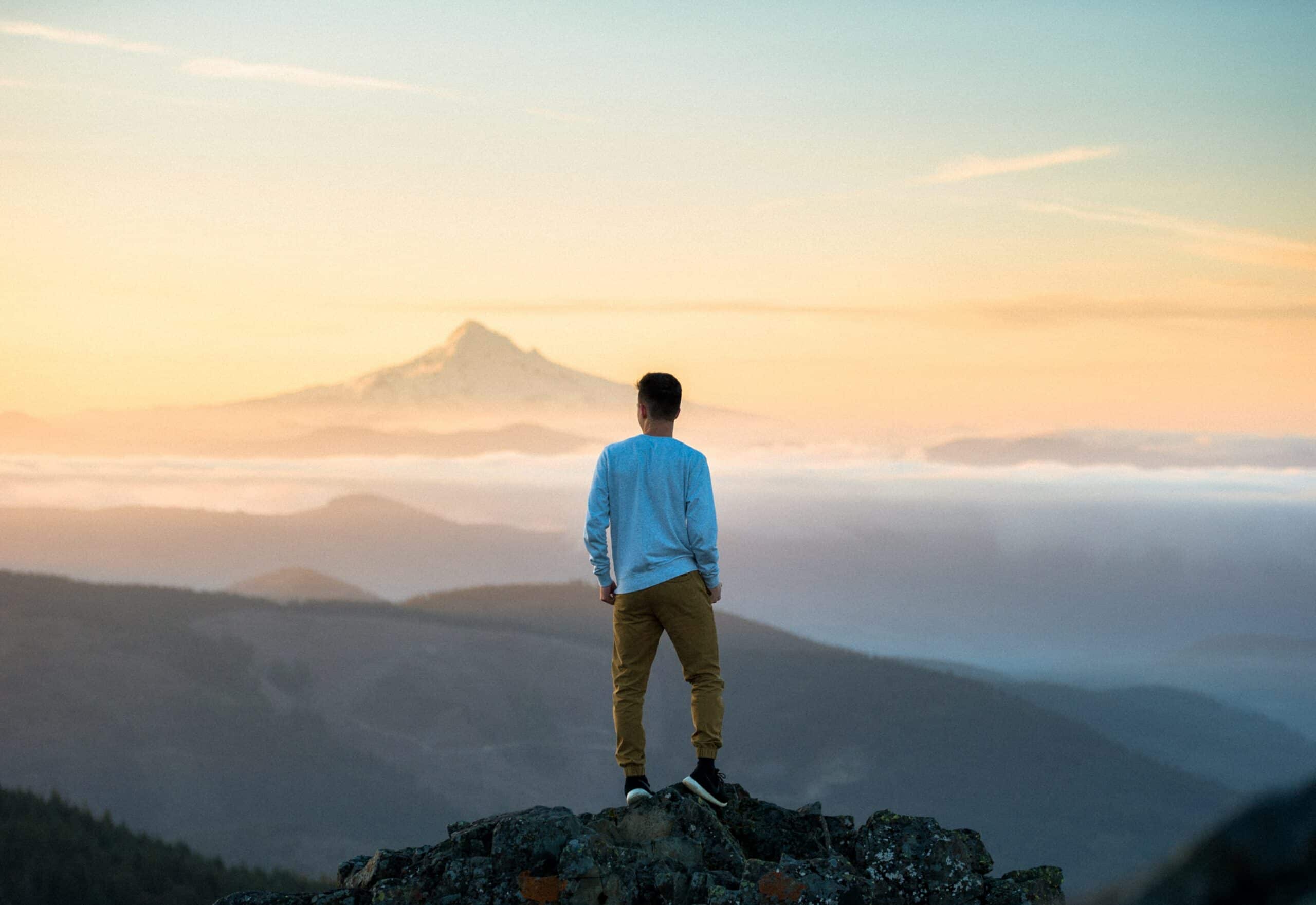 A man standing on top of a mountain looking at the sky.