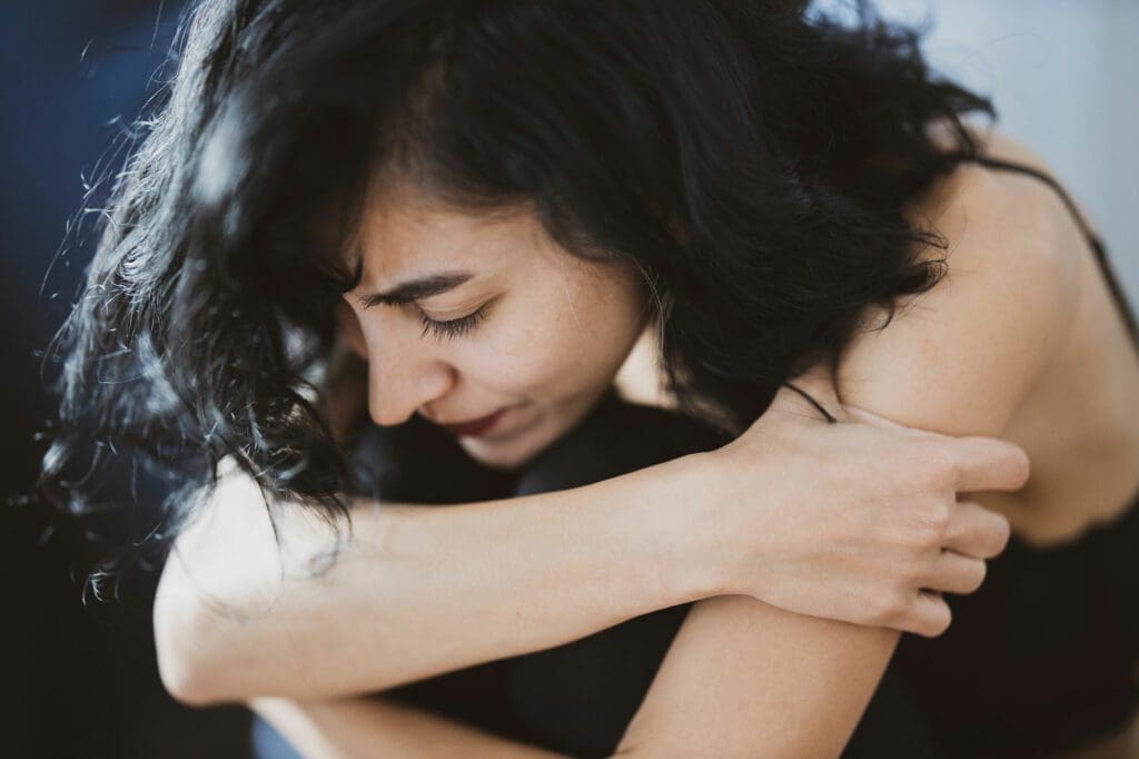 A woman hugging herself with her arms around the neck of another person.