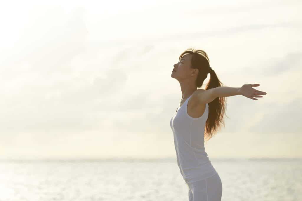 A woman is standing on the beach with her arms outstretched.