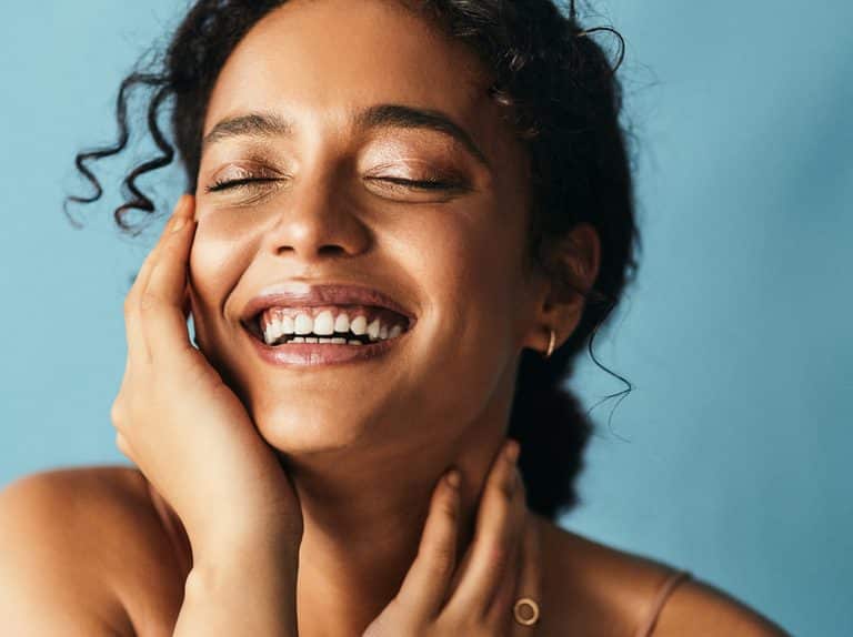 A woman smiling with her hands on her face.