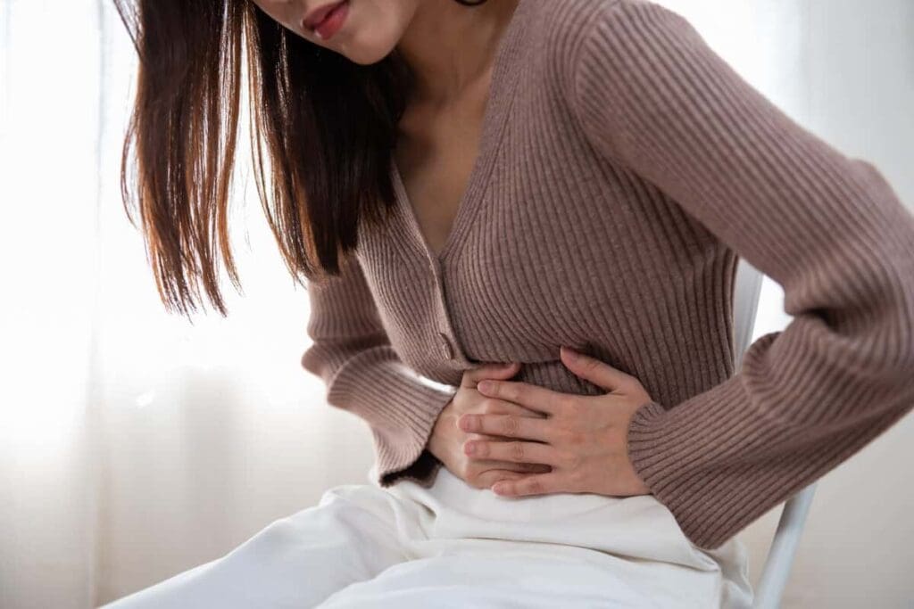 A woman holding her stomach in the middle of a bed.