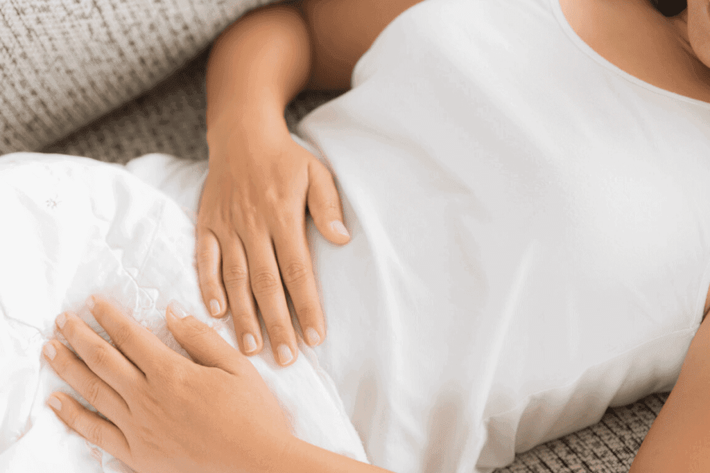 A person is laying on the bed with their hands in her stomach.