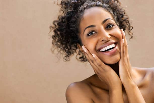 A woman with curly hair smiling and holding her hands to her face.