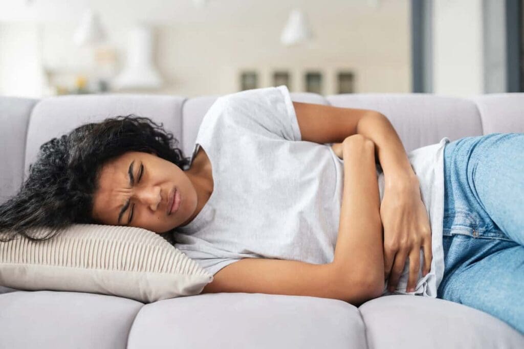 A woman is lying on the couch with her stomach in pain.