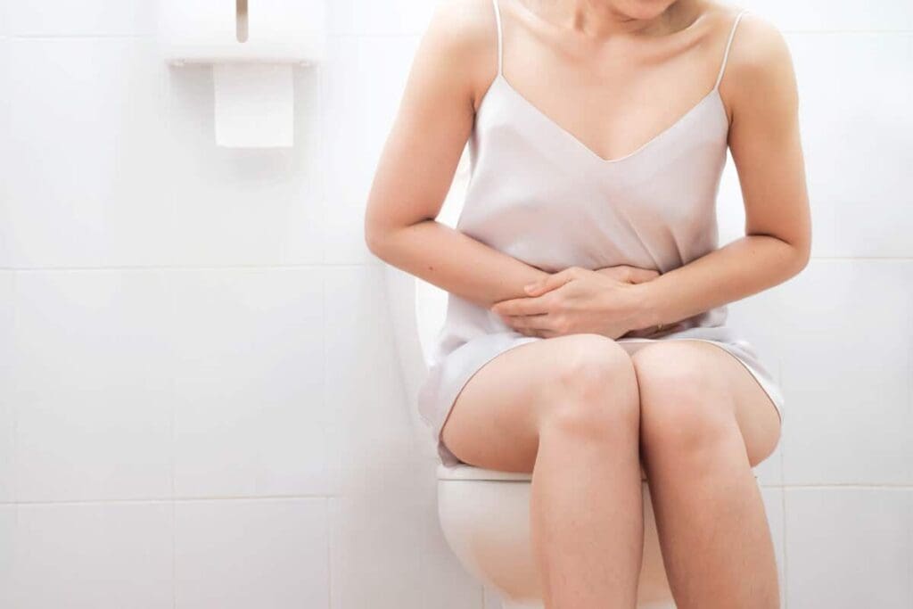 A woman sitting on the toilet with her hands in her stomach.