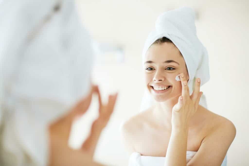 A woman in the mirror putting cream on her face.