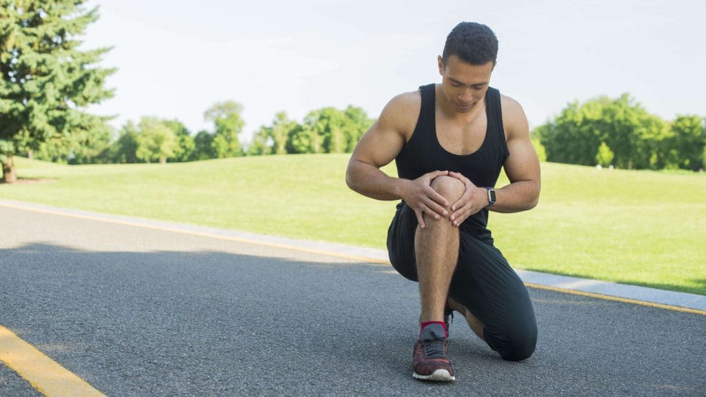 A man kneeling down on the ground holding his knee.