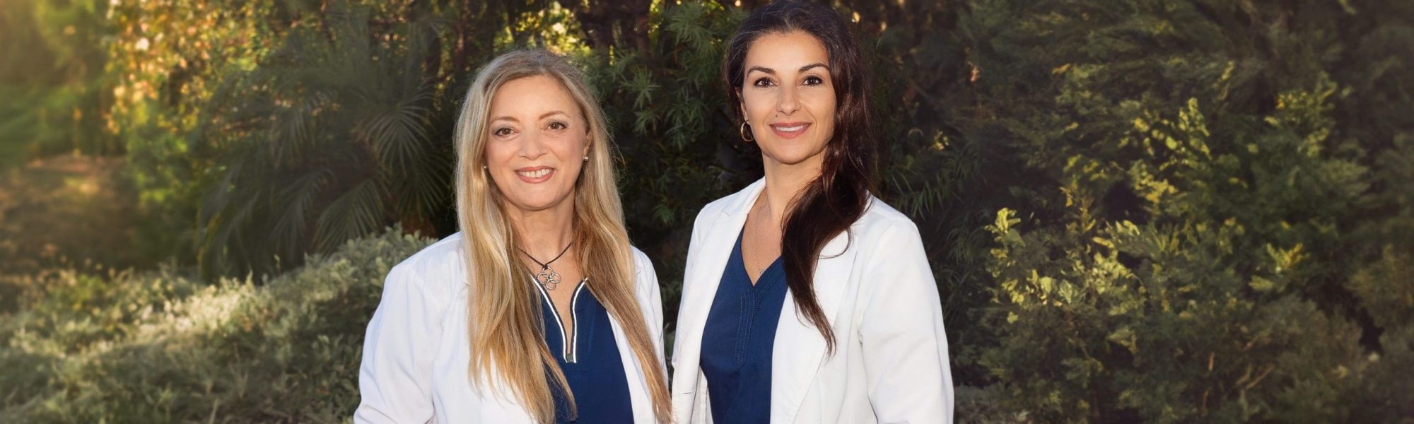 Two women standing next to each other in front of a tree.