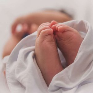 A baby is wrapped in a blanket and holding its feet.